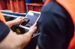 Close up of two workers using tablet computer at factory warehouse. Foremen with colleague using digital tablet in warehouse.