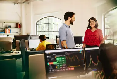 Two colleagues male and female having a chat standing between desks.
