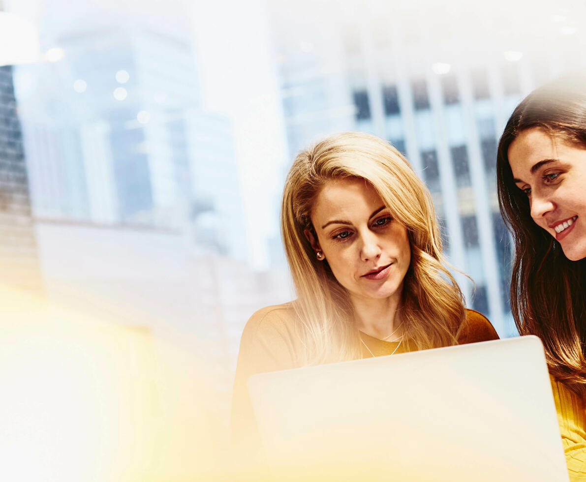 two females working and smiling on their laptops in an office