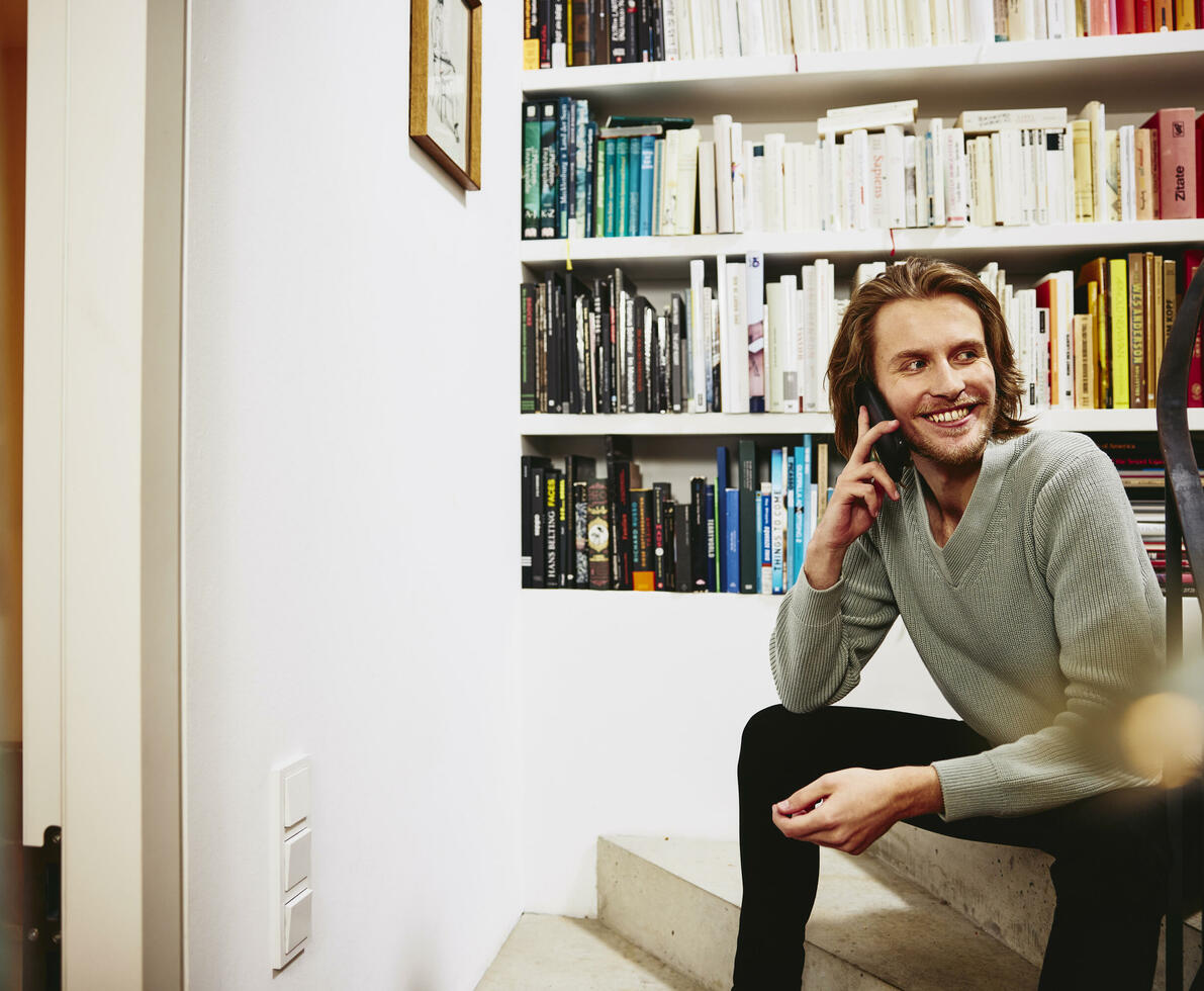 Smiling male sitting on stairs, having a phonecall. bookshelf in background
Smiling male sitting on stairs, having a phonecall. bookshelf in background