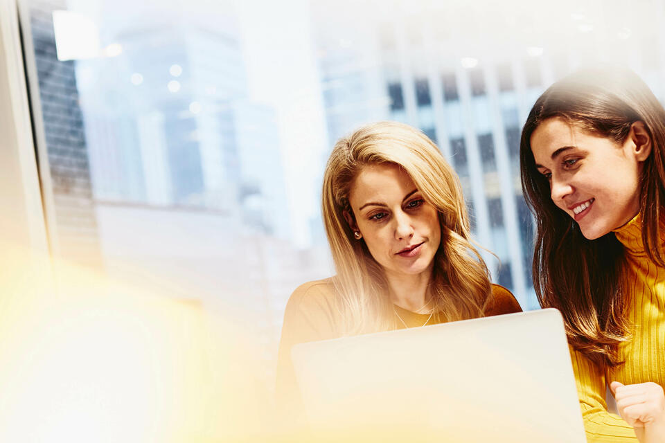 two females working and smiling on their laptops in an office