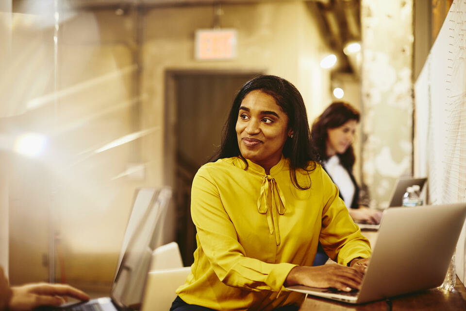 Two smiling women working on their laptop.